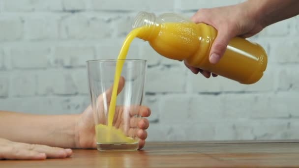 Mother pouring orange juice to glass in boy's hands, slow motion - Footage, Video