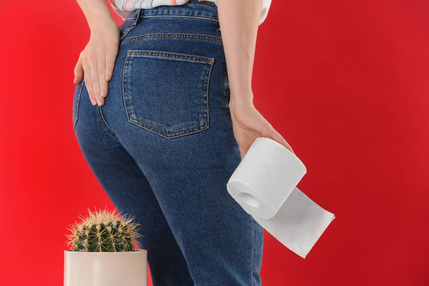 Woman with toilet paper sitting down on cactus against red background, closeup. Hemorrhoid concept - Foto, Imagen