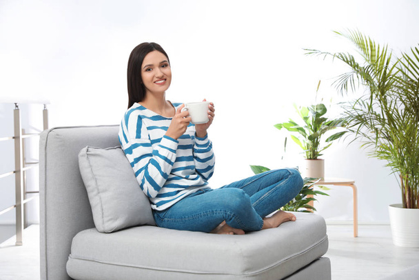 Young woman with cup of drink relaxing on couch at home - Zdjęcie, obraz