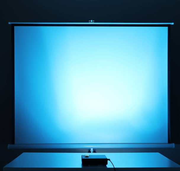 Projetor de vídeo e tela dentro de casa, tonificado em azul claro. Espaço para design
 - Foto, Imagem