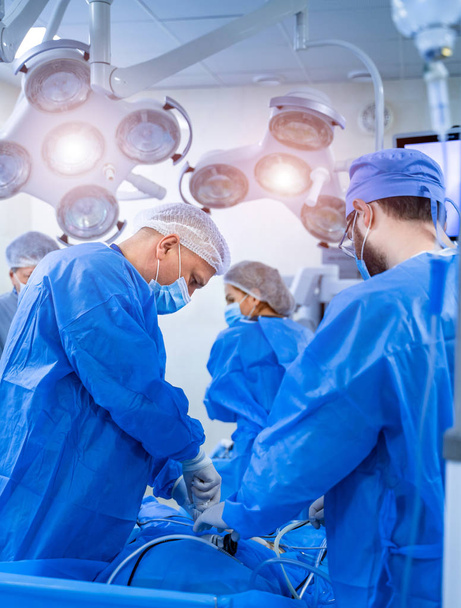 Group of doctors perform an operation to a patient. Surgeons in medical uniform and masks working in the operating room - Valokuva, kuva