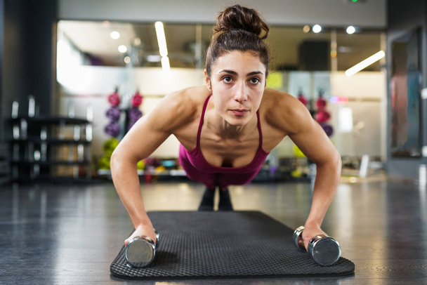 Woman doing push-ups exercise with dumbbell in a fitness workout - Fotografie, Obrázek