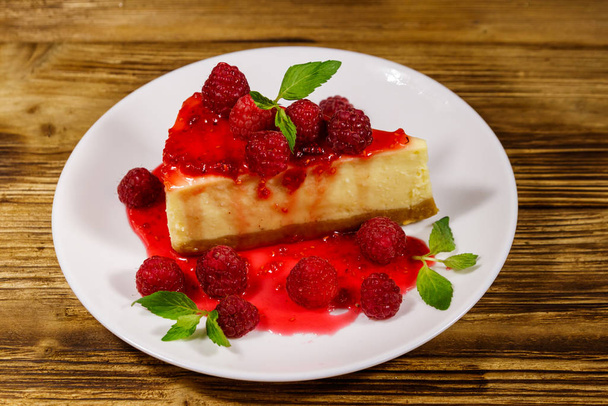 Piece of tasty New York cheesecake with raspberries and raspberry jam in a white plate on wooden table - Foto, Bild