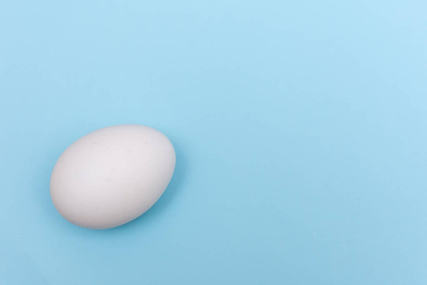 Piso de vacaciones de Pascua poner con huevo blanco sobre un fondo vibrante sólido azul brillante y amarillo con espacio de copia
. - Foto, imagen