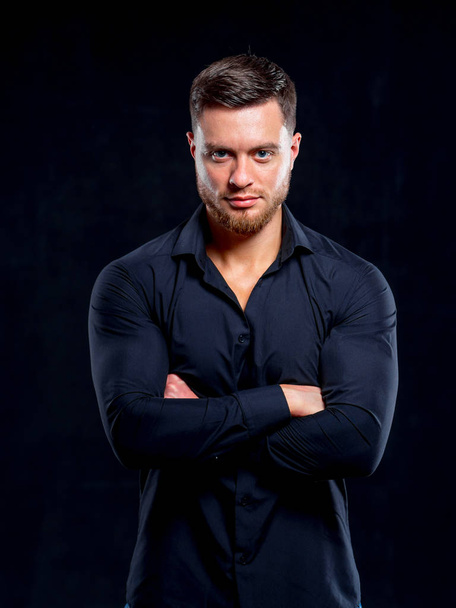 Young man in black shirt smiling isolated on dark background. Standing cross hands. Muscular male, athletic. Fashion portrait - Foto, Bild