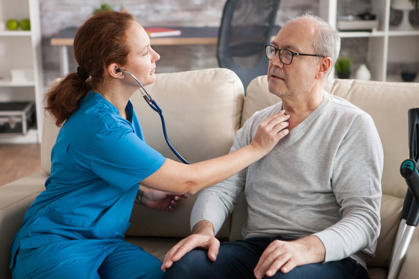 Pretty female nurse using stethoscope to listen the heart of old man - Fotó, kép