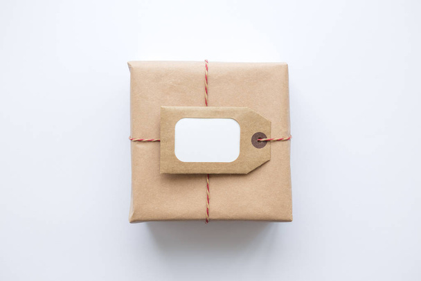 Flat lay of wrapped package with blank tag on white background. Shipping logistics transport minimal creative concept. - 写真・画像
