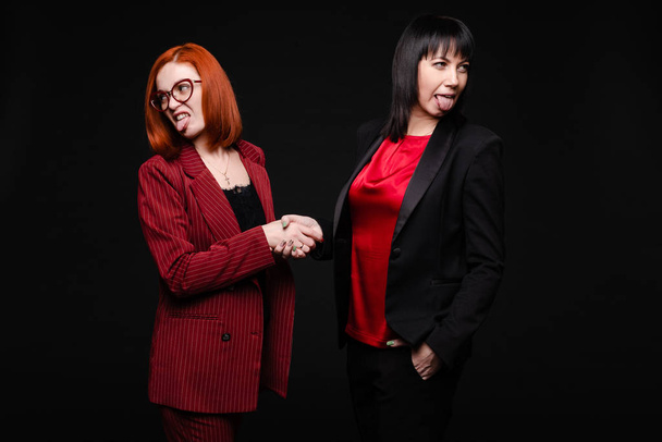 Businesswomen showing disgust while shaking hands.Business partners showing dislike to their business deal. Isolate on black. - Photo, Image