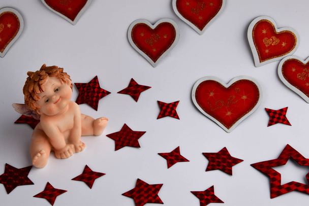 A little cheerful angel sits and smiles, and there are many different sizes of red hearts around - Photo, Image