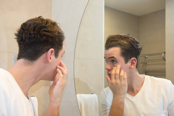 молодий білий чоловік піклується про своє обличчя, дивлячись на дзеркало р
 - Фото, зображення