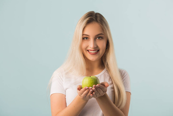 beautiful young woman with a green apple in her hands on a blue background - Photo, Image