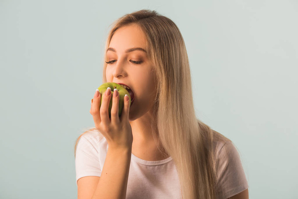 beautiful young woman with a green apple in her hands on a blue background - Fotografie, Obrázek