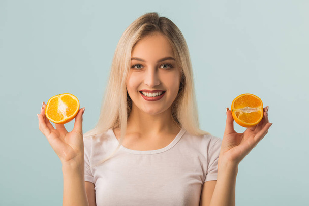 schöne junge Frau mit grünem Apfel und Orange in den Händen auf blauem Hintergrund - Foto, Bild