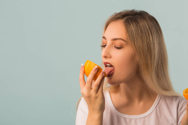 beautiful young woman with green apple and orange in hands on a blue background - Фото, изображение