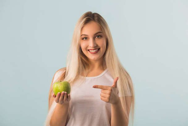 beautiful young woman with a green apple in her hands on a blue background - Foto, afbeelding