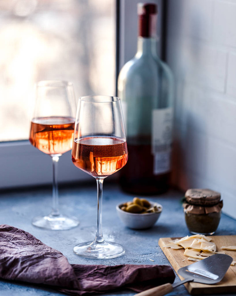 Δύο ποτήρια ροζέ κρασί σε μπλε φόντο με φέτες τυριού και ελιές. - Φωτογραφία, εικόνα