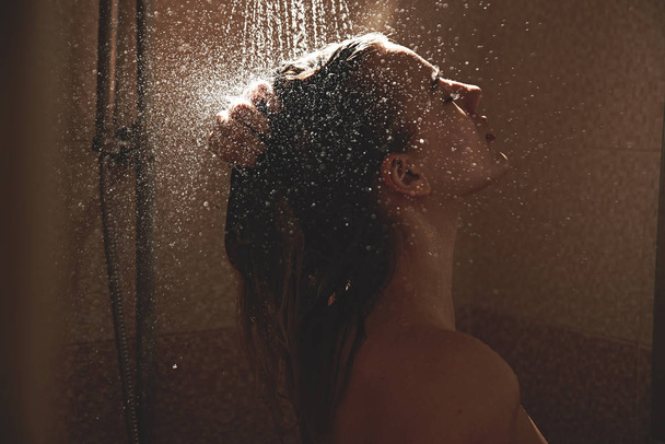 Authentic naked blonde girl takes a shower, washes sexy body with water drops in bathroom, enjoys with eyes closed - Foto, Bild