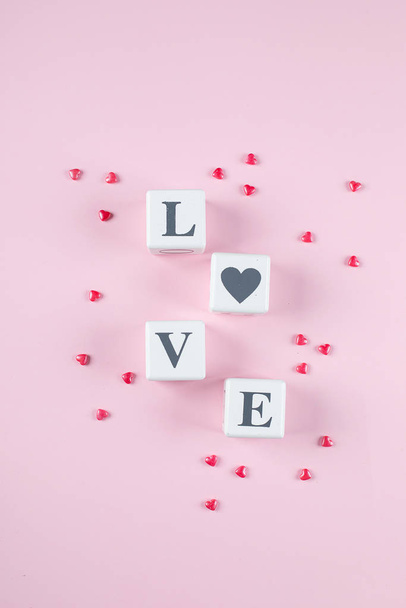 Liefdesboodschap geschreven in witte houten blokken op roze achtergrond. Roze snoepharten. Vlakke lay, bovenaanzicht - Foto, afbeelding
