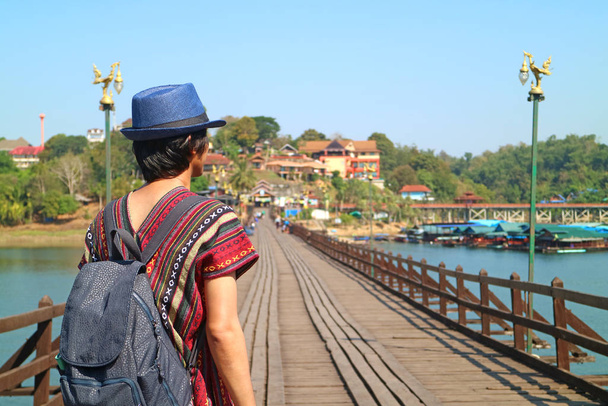 Back of a Traveler with Blurry Mon Bridge, the Iconic Landmark of Sangkhlaburi, Thailand in Background - Foto, Imagen