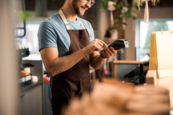 Happy male waiter in apron with card reader - Photo, Image