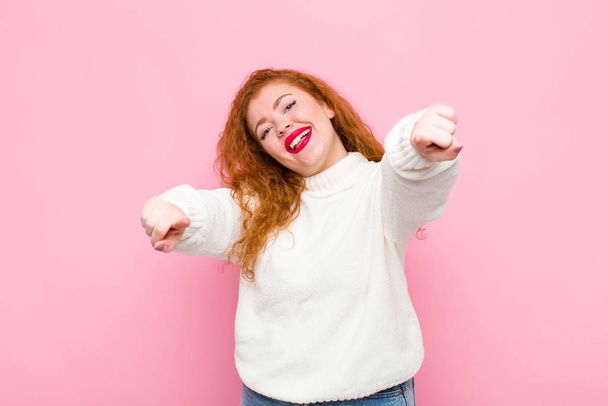 young red head woman feeling happy and confident, pointing to camera with both hands and laughing, choosing you against pink wall - Foto, Bild