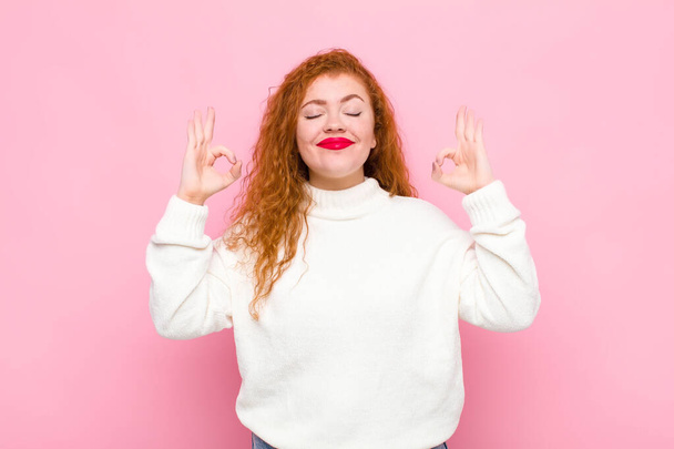young red head woman looking concentrated and meditating, feeling satisfied and relaxed, thinking or making a choice against pink wall - Foto, imagen