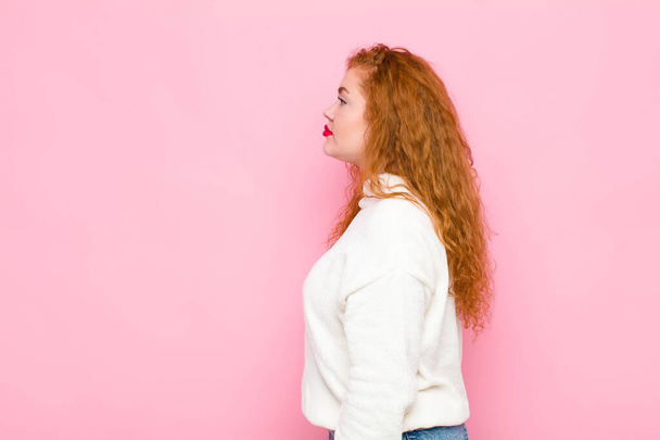 jovem mulher cabeça vermelha na visão de perfil olhando para copiar espaço à frente, pensando, imaginando ou sonhando acordado contra a parede rosa
 - Foto, Imagem