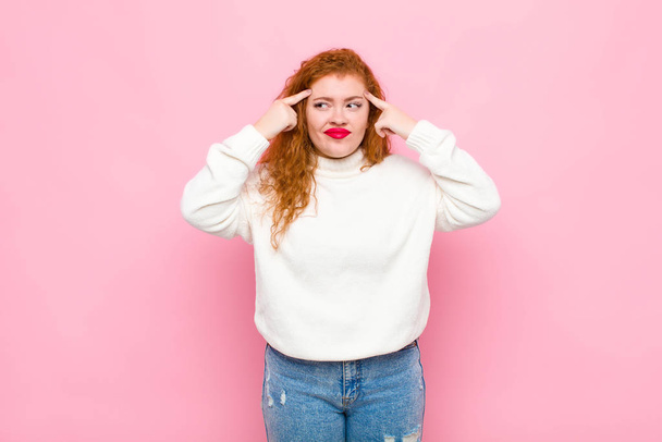 young red head woman looking concentrated and thinking hard on an idea, imagining a solution to a challenge or problem against pink wall - Fotoğraf, Görsel