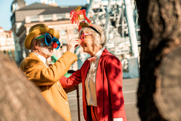 Happy old man and woman in clown accessories outdoors - Foto, Imagen