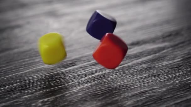 Three multi-colored game dice fall on a black textured old wooden table. Bounce and spin. Red, yellow and blue - Filmagem, Vídeo