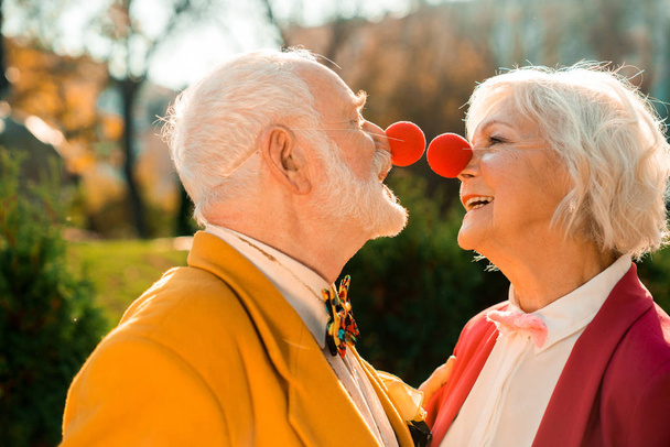 Happy old man and woman with red noses connecting them - 写真・画像