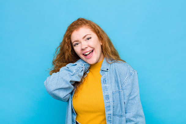 young red head woman laughing cheerfully and confidently with a casual, happy, friendly smile against blue wall - Fotó, kép