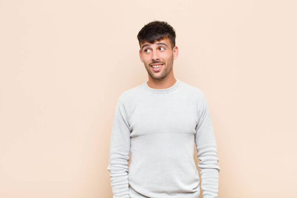 young handsome man feeling shocked, happy, amazed and surprised, looking to the side with open mouth against warm wall - Foto, Bild
