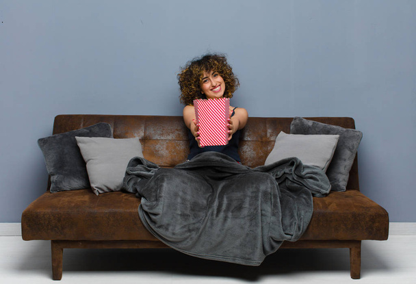 young pretty woman at home  and sitting on a sofa with a popcorns bucket. cinema concept - Photo, Image