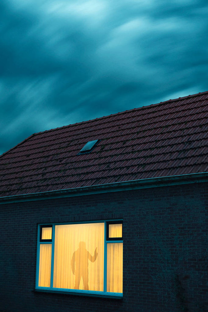 Inbreker met pistool in onheilspellend huis met verlichte ruit on - Foto, afbeelding