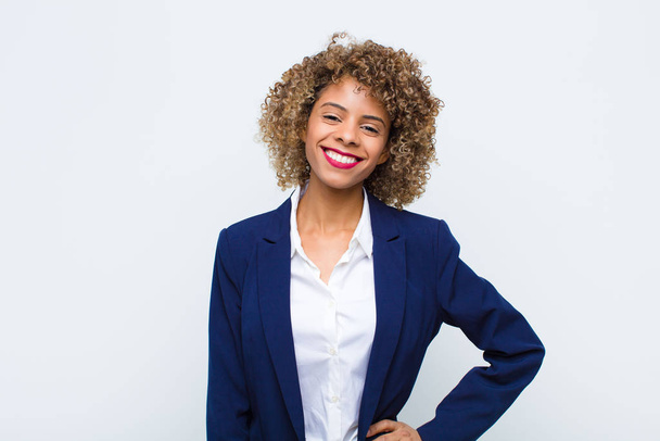 mladá žena Afroameričanka šťastně se usmívá s rukou na boku a sebevědomý, pozitivní, hrdý a přátelský postoj proti ploché zdi - Fotografie, Obrázek