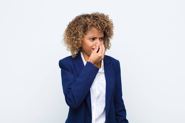 young woman african american feeling disgusted, holding nose to avoid smelling a foul and unpleasant stench against flat wall - Photo, image