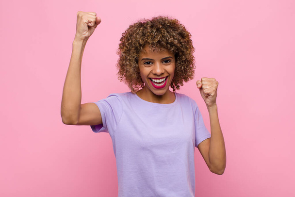 young african american woman shouting triumphantly, looking like excited, happy and surprised winner, celebrating against pink wall - Photo, image