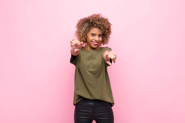 young african american woman feeling happy and confident, pointing to camera with both hands and laughing, choosing you against pink wall - Foto, afbeelding