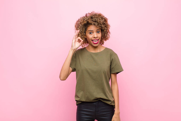 young african american woman feeling successful and satisfied, smiling with mouth wide open, making okay sign with hand against pink wall - Foto, imagen