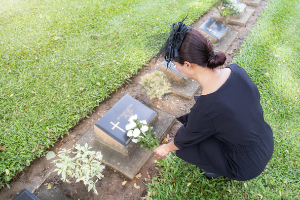 Jeune femme en deuil posant des fleurs blanches sur sa tombe familiale dans un beau cimetière vert
. - Photo, image