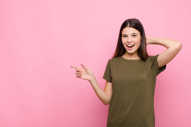 young pretty woman laughing, looking happy, positive and surprised, realizing a great idea pointing to lateral copy space against pink wall - Foto, Imagem