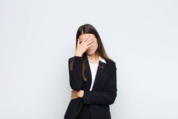 young businesswoman looking stressed, ashamed or upset, with a headache, covering face with hand against white wall - Foto, Bild