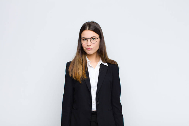 jonge zakenvrouw die zich verward en twijfelachtig voelt, zich afvraagt of probeert te kiezen of een beslissing neemt tegen de witte muur - Foto, afbeelding
