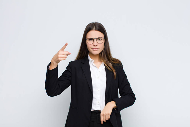 young businesswoman pointing at camera with an angry aggressive expression looking like a furious, crazy boss against white wall - Photo, Image