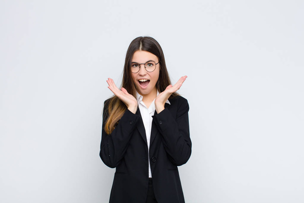 young businesswoman feeling shocked and excited, laughing, amazed and happy because of an unexpected surprise against white wall - Fotoğraf, Görsel
