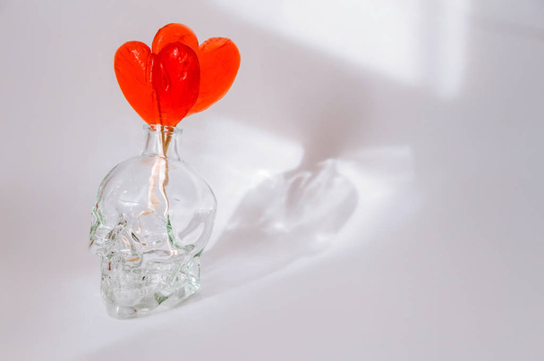 két szív alakú cukorka áll egy koponya alakú kancsóban fehér alapon - Fotó, kép