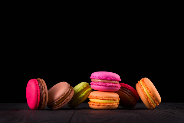 French colorful macaroons in row on wooden table isolated on black - Foto, Imagem