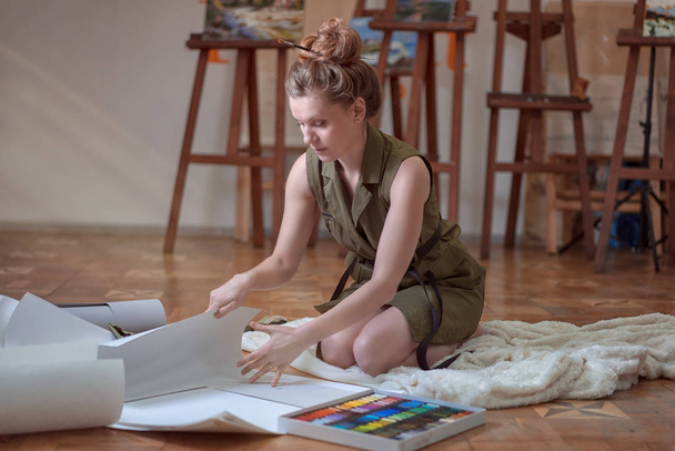 Artista mulher senta-se no chão e selecione papéis para tintas no estúdio de arte
. - Foto, Imagem