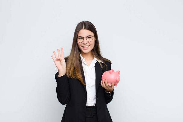 young pretty woman smiling and looking friendly, showing number four or fourth with hand forward, counting down with a piggy bank - Foto, Bild